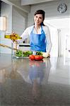 Young smiling woman pouring olive oil into a salad