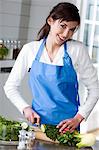 Young smiling woman making a salad, chopping cucumber