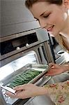 Young woman putting string beans into an oven
