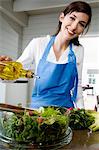 Young smiling woman pouring olive oil into a salad