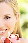 Portrait of a young  blond woman smiling, holding petals, outdoors