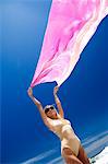 Young woman in swimming costume holding pink pareo in wind