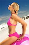 Young woman in pink bikini on the beach, sitting on a large ball