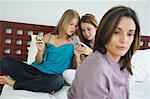 2 teenage girls sitting on bed, using mobile phones, thinking woman in foreground