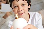 Portrait of a little boy holding a candle, sister in background, indoors