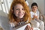 Christmas day, portrait of a little girl holding a present, little boy in background, indoors