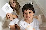 Christmas day, portrait of a little boy holding a candle, girl in background reading a card, indoors