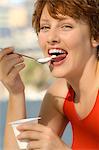 Portrait of a young smiling woman eating yogurt