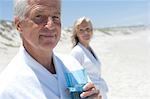 Paar im Bademantel am Strand, Mann mit Glas Wasser im Vordergrund