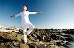 Senior woman doing yoga on seaside rocks