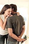 Man hiding bunch of flowers behind his back, facing smiling woman