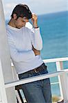 Young thinking man leaning against wall on a terrace, sea in background