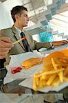Milieu adulte homme d'affaires ayant des hamburger et des frites françaises, à l'aide d'ordinateur portable