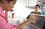 Businesswoman checking in laptop with businessman sitting in background