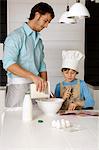 Mid adult man making a cake with his son in the kitchen