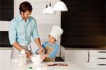 Mid adult man making a cake with his son in the kitchen