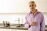 Portrait d'un homme d'âge mûr tenant un verre d'eau dans la cuisine
