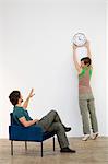 Mid adult man looking at his wife mounting a clock on the wall