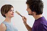 Close-up of a mid adult man applying paint on a young woman's nose