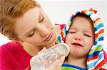 Close-up of a young woman feeding from a baby bottle to her crying son