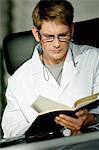 Close-up of a male doctor sitting at a desk and reading a notebook