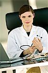 Portrait of a female doctor sitting at a desk and holding a stethoscope in her office