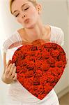 Young woman holding a heart shape gift and puckering her lips