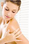 Close-up of a young woman applying moisturizer on her shoulder