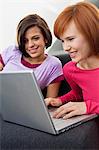 Two young women using a laptop and smiling