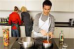 Young man cooking food with two young women standing behind him