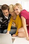 Two young women and a young man using a laptop and smiling