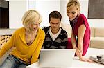 Jeune homme avec deux jeunes femmes à la recherche à un ordinateur portable