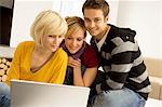 Two young women and a young man sitting in front of a laptop and smiling