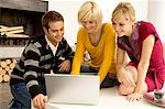 Jeune homme avec deux jeunes femmes à la recherche à un ordinateur portable et souriant