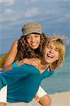 Girl riding piggyback on a teenage boy on the beach