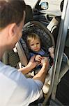 Man fastening his son on a baby seat in a car