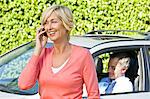 Woman talking on a mobile phone and her husband in a car in the background