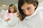 Close-up of a girl wrapped in a blanket with her sister talking on mobile phone in the background