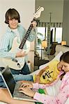 Boy playing a guitar and girl working on a laptop