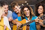 Man sitting with his friends and playing a guitar