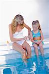 Femme avec sa fille assise au bord de la piscine