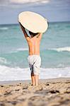 Rear view of a boy holding a body board over his head