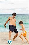 Garçon jouant au soccer avec son père sur la plage