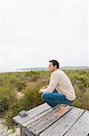 Man crouching on a boardwalk and thinking