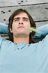 Man lying on a boardwalk and thinking with husk of wheat in his mouth