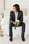 Groom sitting on the bed and holding a lily flower