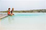 Two girls sitting on a platform at an infinity pool