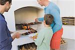 Two men with a boy cooking kebab at fireplace