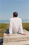 Rear view of a man sitting on a boardwalk