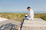 Man sitting on a boardwalk and reading a book